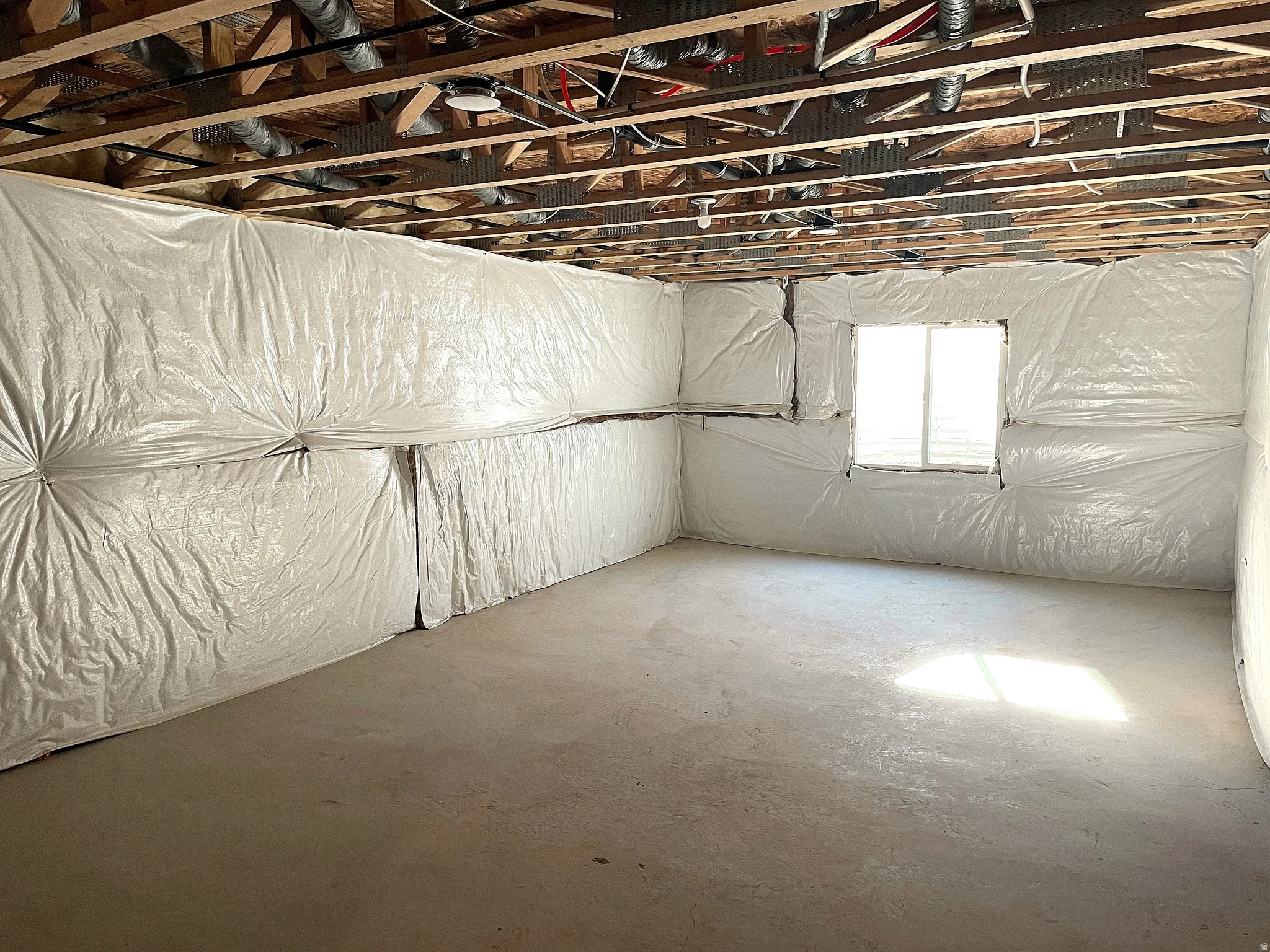 Unfinished basement space featuring exposed wood joists, concrete flooring, insulated walls, and a single window