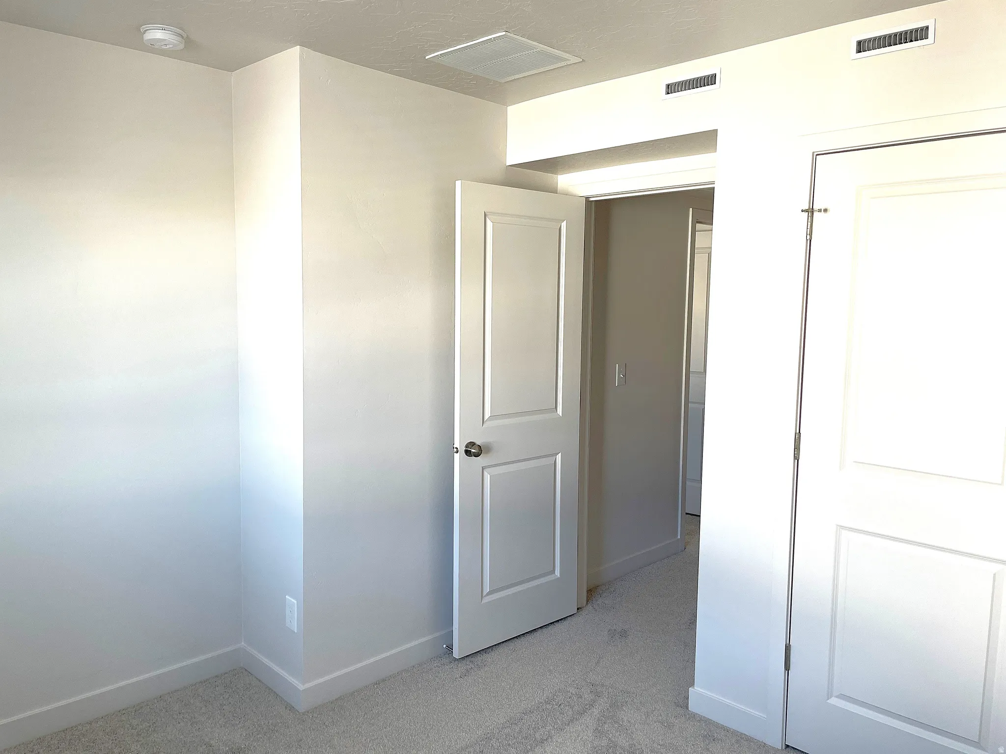 Neutral tone wall paint, light-colored carpeting, white trim, white paneled doors, and recessed ceiling vents