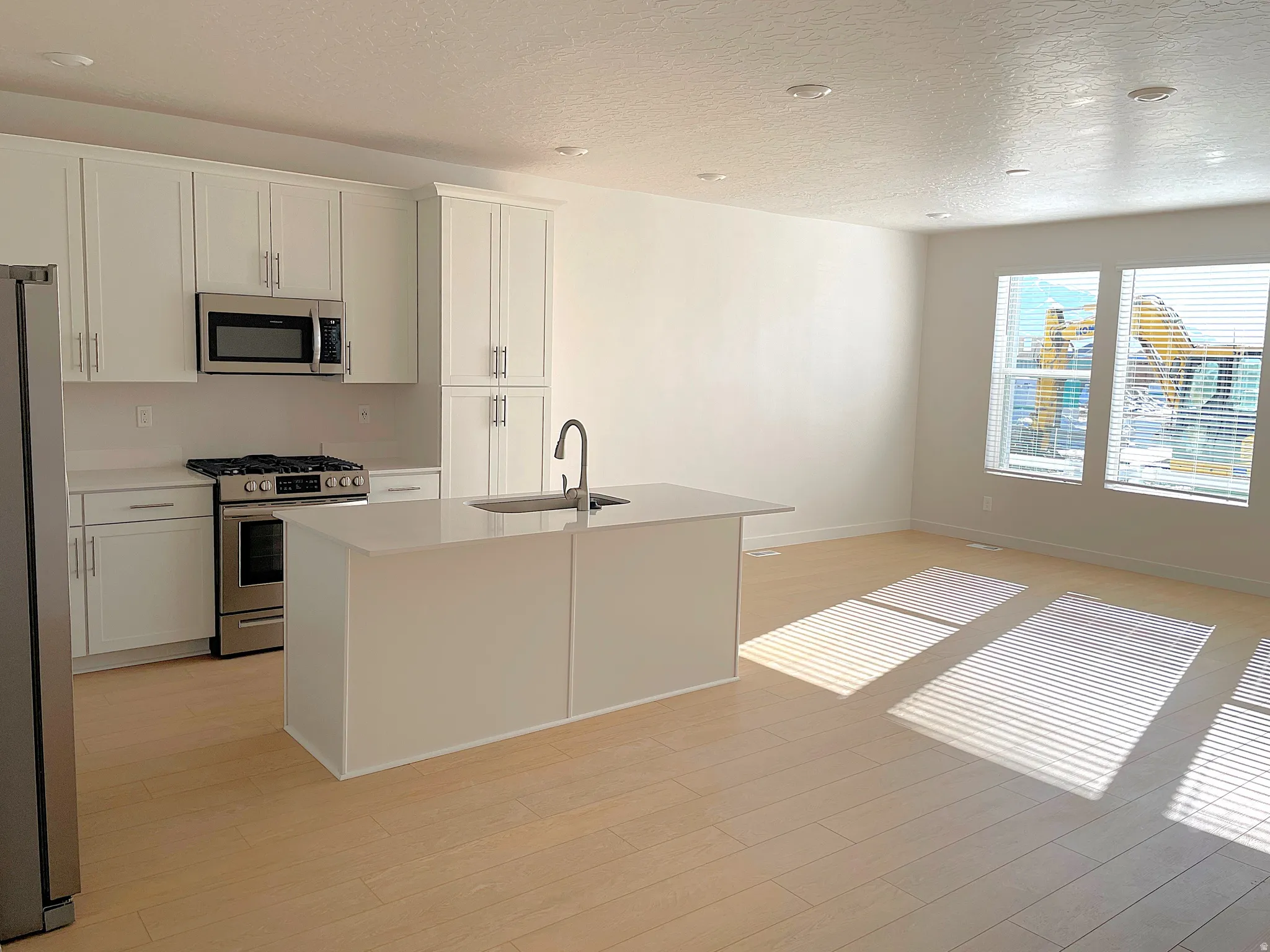 Open-concept kitchen featuring white cabinetry, stainless steel appliances, a center island with an undermount sink, and wood-finish flooring