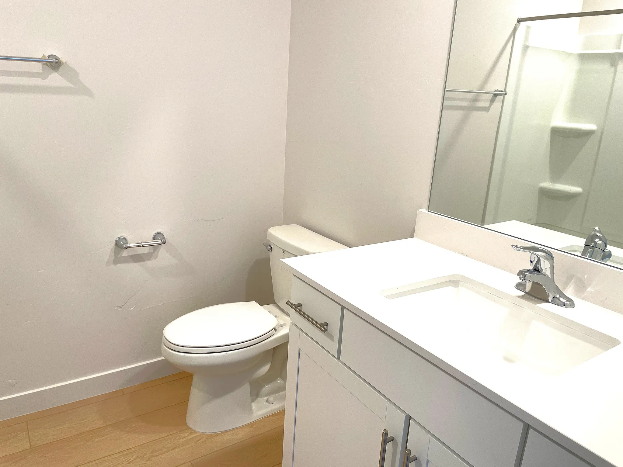 White vanity with integrated sink, chrome faucet, and wood-finish flooring
