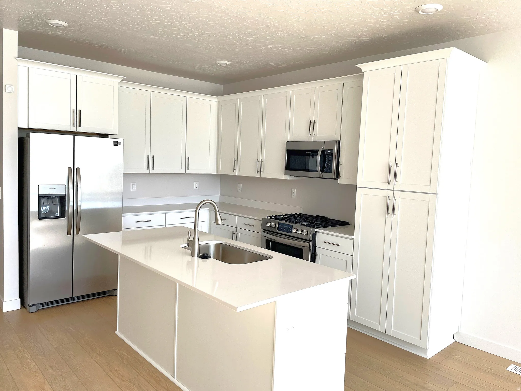 Kitchen featuring a large island with an integrated stainless steel sink, stainless steel appliances, extensive white cabinetry, and wood-finish flooring