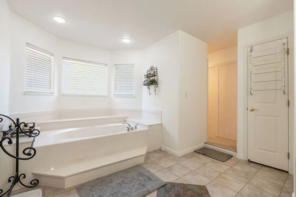 Recessed lighting, tiled flooring, built-in soaking tub, window blinds, and white interior doors