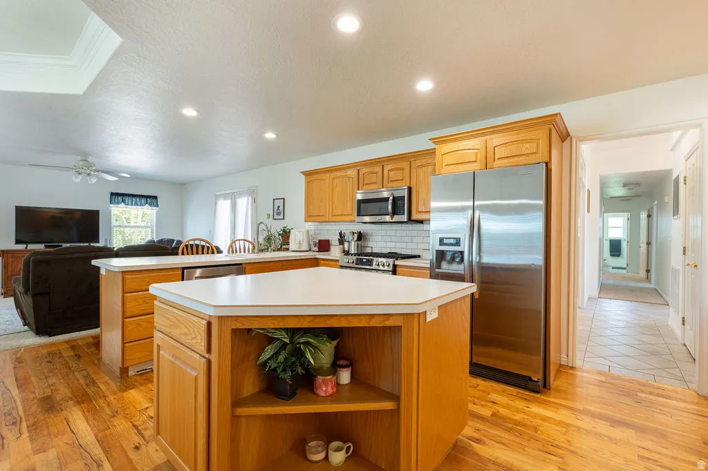 Open-concept kitchen featuring wood-finish flooring, stainless steel appliances, and wood cabinetry with a white tile backsplash