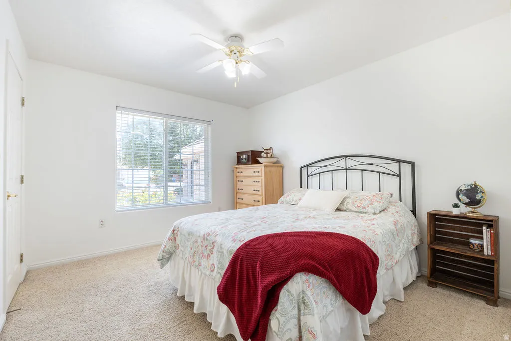 Carpeted flooring with a ceiling fan, a window with blinds, and white walls