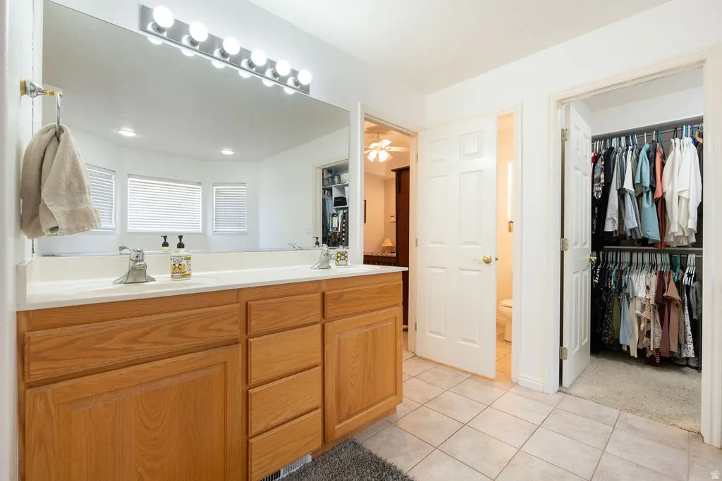 Dual vanity with a large mirror, wood-finish cabinetry, and tiled flooring