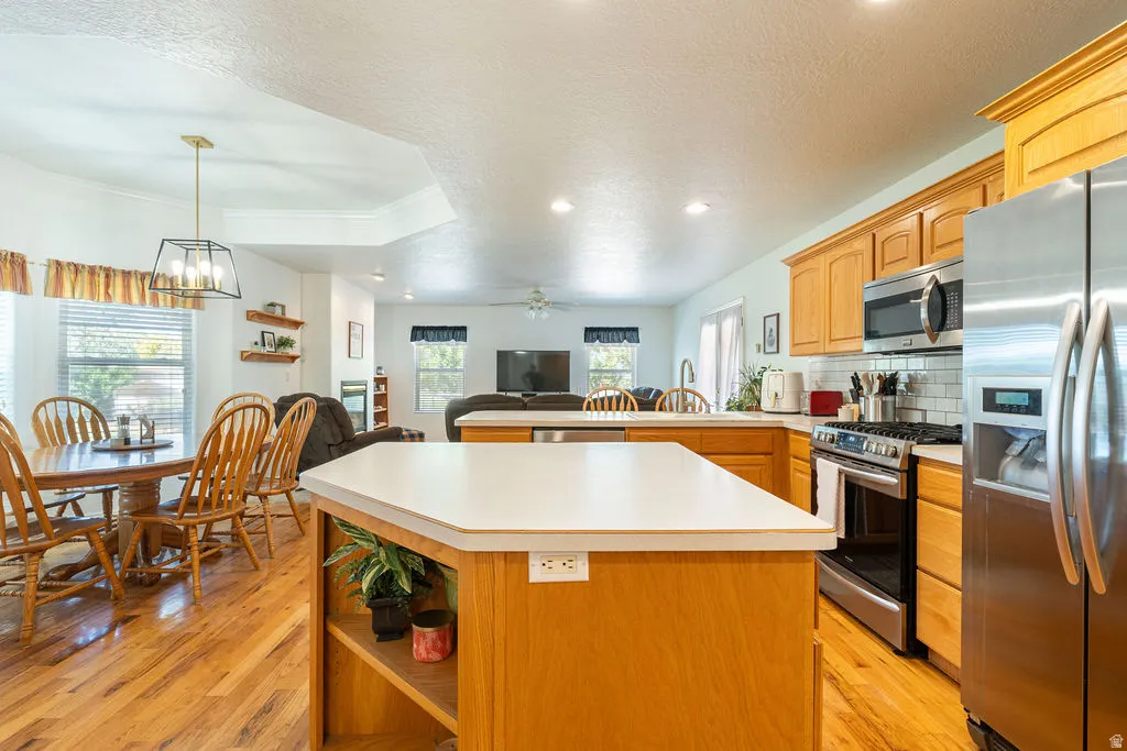 Kitchen island with built-in shelving, stainless steel appliances, and wood-finish flooring extending into the dining area