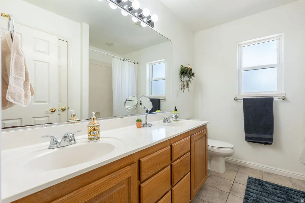 Double vanity with a white countertop and chrome fixtures, wood-finish cabinetry, a large wall-mounted mirror, and a window with frosted glass