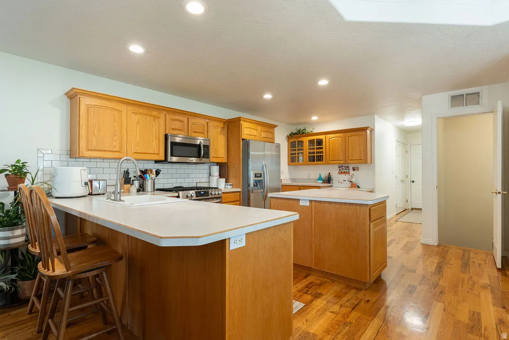 Kitchen featuring wood-finish cabinetry, stainless steel appliances, a subway tile backsplash, recessed lighting, and wood-finish flooring