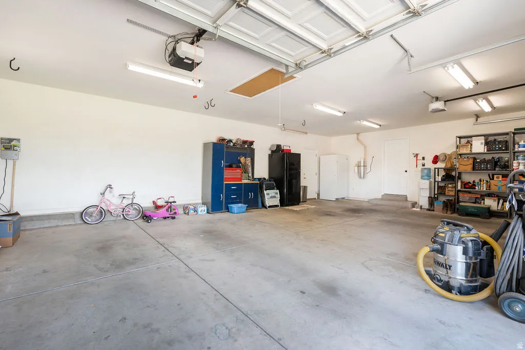 Attached two-car garage with concrete flooring, multiple fluorescent light fixtures, and overhead garage door mechanism