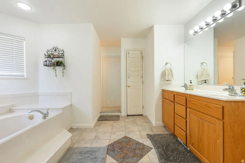Dual vanity with wood-finish cabinetry, a built-in soaking tub, a large mirror, and recessed lighting