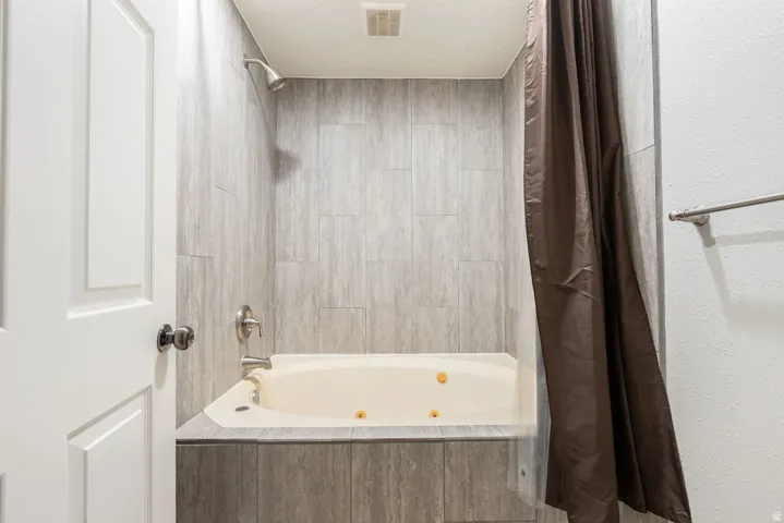 Tiled shower surround with a built-in jetted tub, wall-mounted showerhead, and a brushed nickel faucet