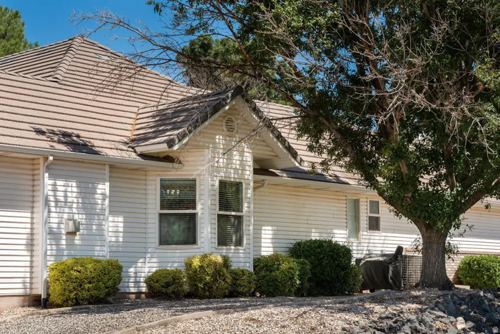 Beige tile roof, white horizontal siding, bay window, landscaped bushes, and gravel ground cover