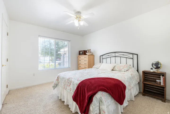 Carpeted flooring with a ceiling fan, a window with blinds, and white walls