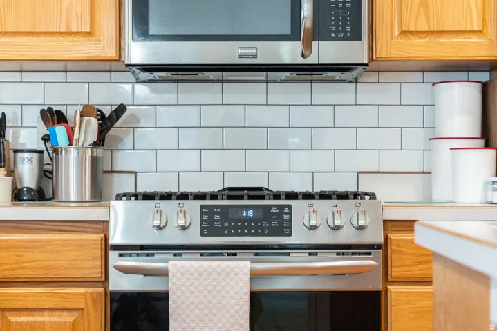 Stainless steel range, stainless steel microwave, light wood-finish cabinetry, subway tile backsplash, and light-toned countertops