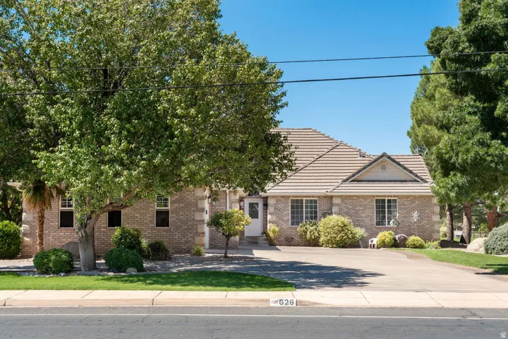 Brick exterior with a tiled roof, mature landscaping, and an expansive paved driveway