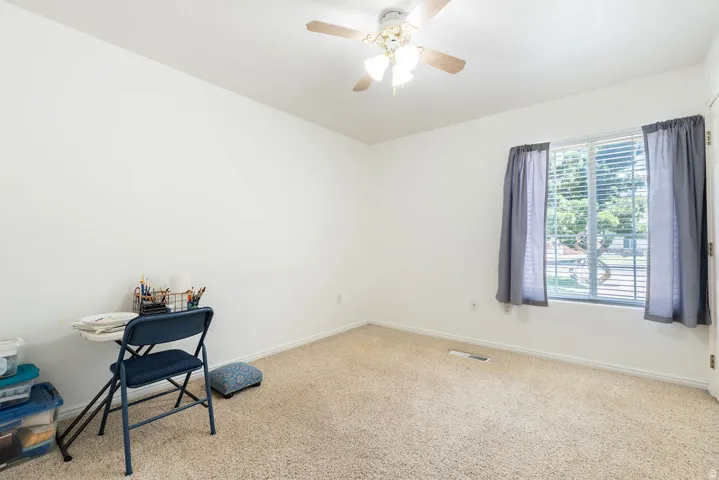 Light-colored carpeting, a window with horizontal blinds, and a ceiling fan with integrated lighting