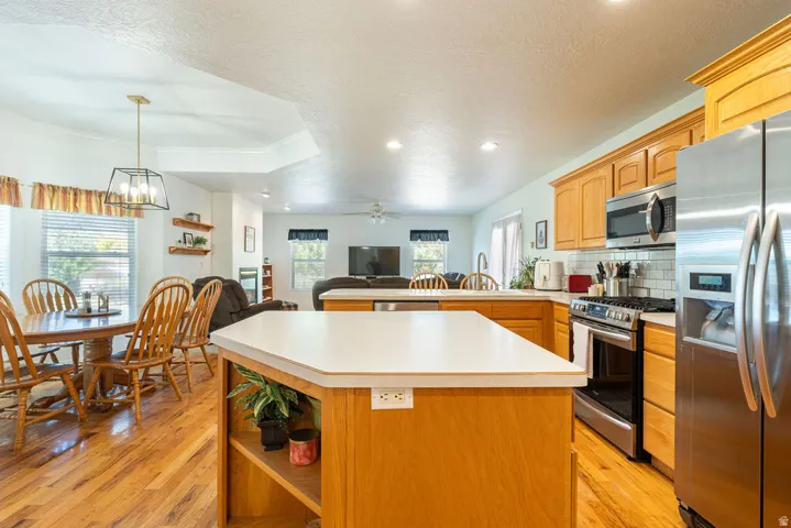 Kitchen island with built-in shelving, stainless steel appliances, and wood-finish flooring extending into the dining area