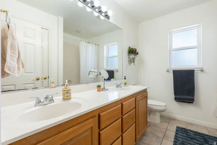 Double vanity with a white countertop and chrome fixtures, wood-finish cabinetry, a large wall-mounted mirror, and a window with frosted glass