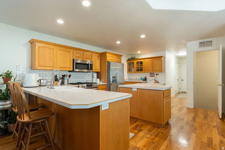 Kitchen featuring wood-finish cabinetry, stainless steel appliances, a subway tile backsplash, recessed lighting, and wood-finish flooring