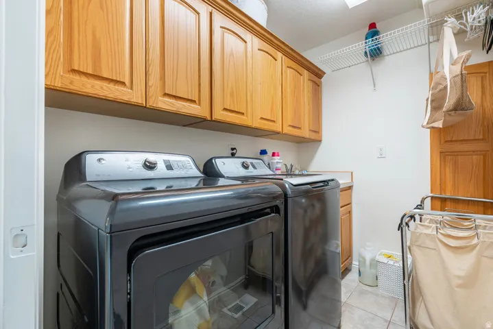 Dedicated laundry room featuring side-by-side washer and dryer with dark stainless steel finish, abundant wood cabinetry storage above, and tile flooring