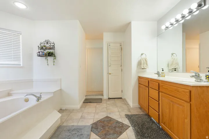 Dual vanity with wood-finish cabinetry, a built-in soaking tub, a large mirror, and recessed lighting