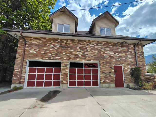 Brick exterior featuring two dormer windows, two garage doors, and a side entry door