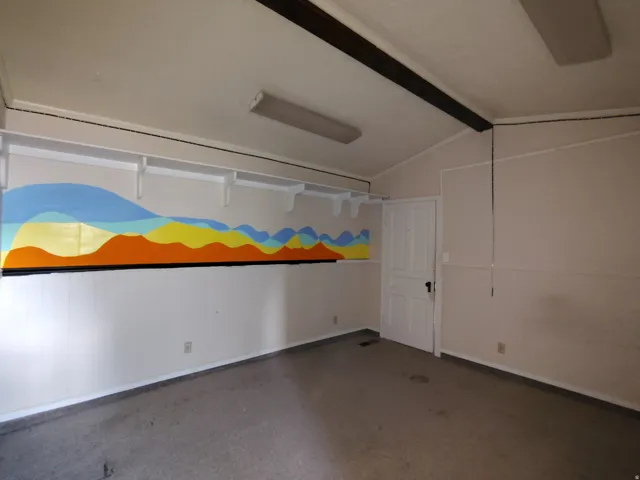 Vaulted ceiling with exposed beam, wall-mounted shelving, wainscoting, and a paneled door