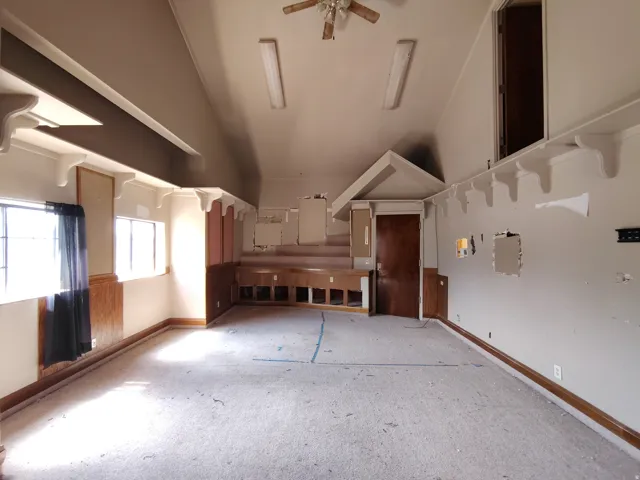 Spacious room featuring multiple windows, wood-panel wainscoting, built-in shelving, and a ceiling fan