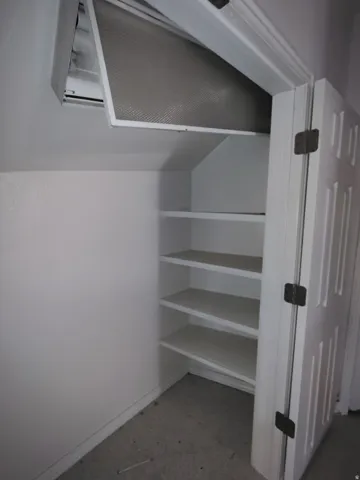 Built-in shelving with four tiers, white paneled door, and exposed air handling unit