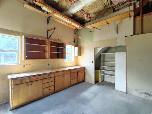 Extensive built-in cabinetry with a long countertop, dual windows, overhead shelving, and a separate storage alcove with shelving