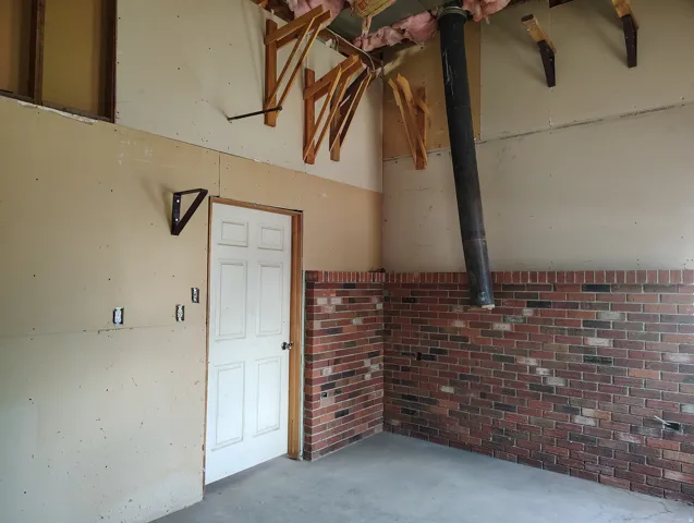 Exposed ceiling joists with insulation, partial brick wall, concrete flooring, and a six-panel interior door