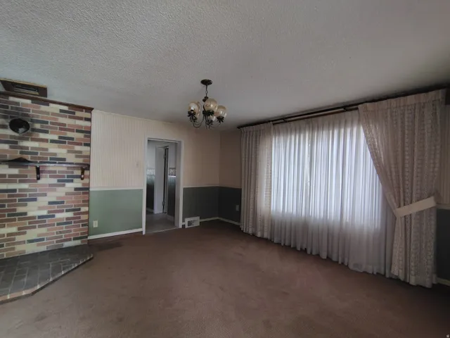 Brick fireplace with hearth, wall-to-wall carpeting, and a multi-light chandelier