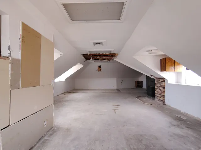 Expansive attic space featuring exposed framing, multiple skylights, and a brick accent wall