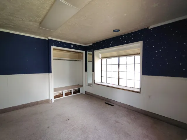 Bedroom featuring two-tone wall treatment with navy upper walls and white lower walls, large multi-pane window with natural light, built-in closet with shelving, and carpeted flooring throughout