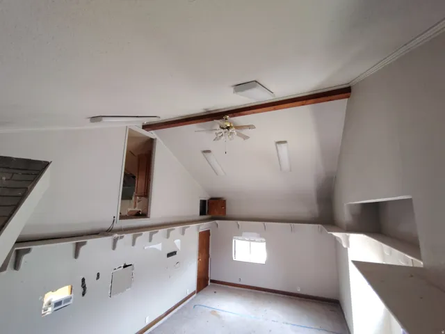 Vaulted ceiling with exposed wood beam, ceiling fan, and fluorescent lighting