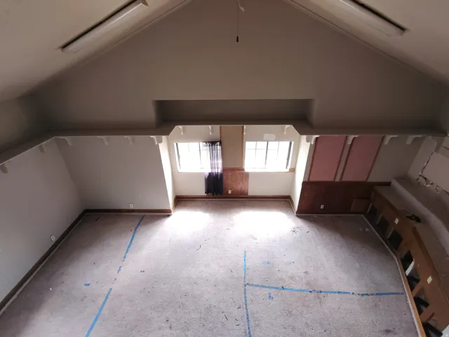 Vaulted ceiling with exposed beams, multiple windows, wood-finish wall paneling, and built-in cabinetry