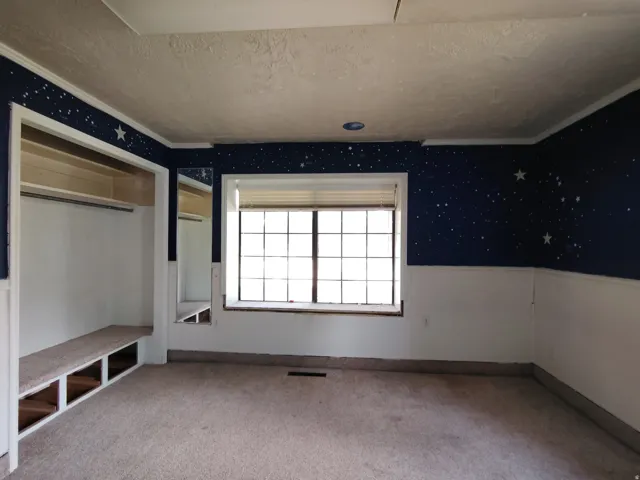 Built-in closet with shelving and hanging rod, window with blinds, carpet flooring, and crown molding