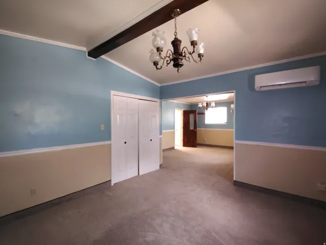 Carpeted interior space featuring a beamed ceiling, chandelier lighting, bi-fold closet doors, and a wall-mounted AC unit