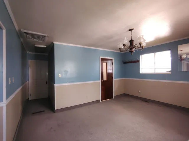 Spacious room featuring carpeting, two-tone wall paint with chair rail molding, a window, and an overhead chandelier