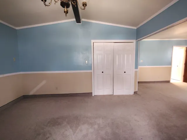 Vaulted ceiling with a chandelier, bi-fold closet doors, two-tone wall treatment, and carpeting