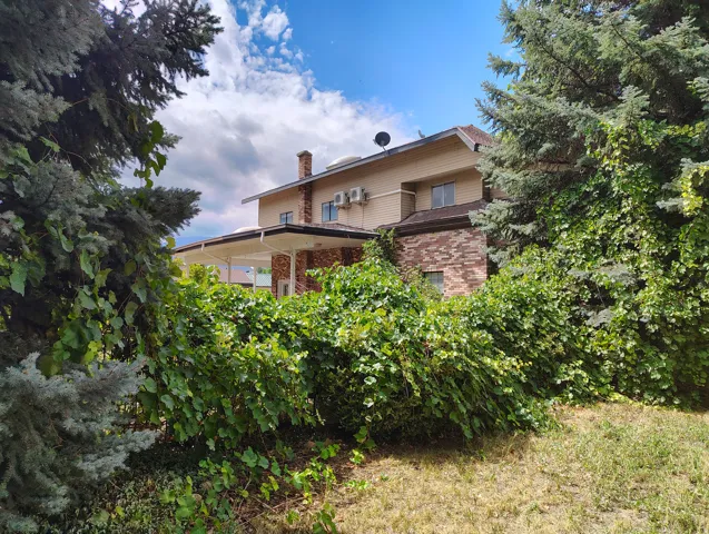 Two-story exterior with brick and siding accents, covered patio, and established perimeter trees