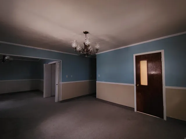 Spacious room featuring wall-to-wall carpeting, two-tone wall paint with chair rail molding, a chandelier, and a dark wood door with a frosted glass insert