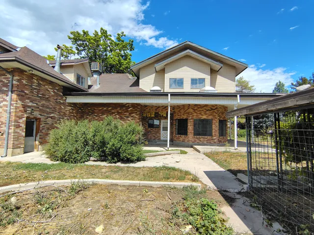 Multi-level exterior with brick and siding finishes, featuring a covered entry, mature landscaping, and a fenced side yard