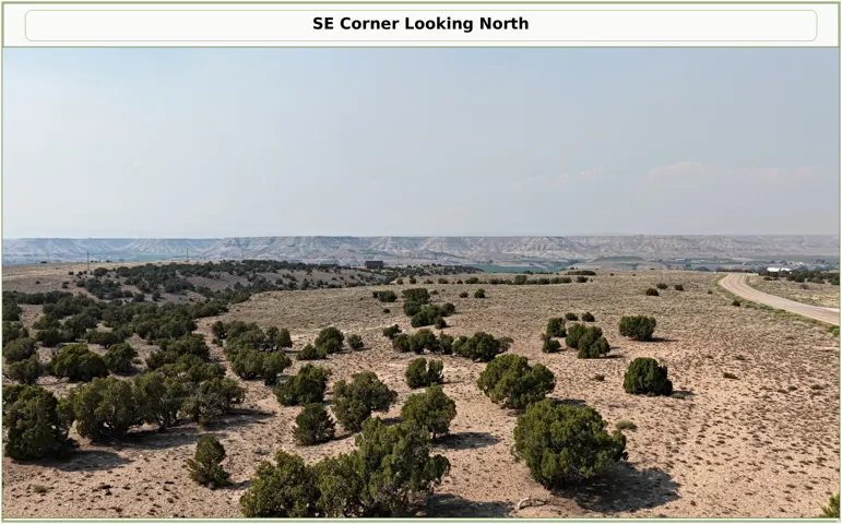 Expansive undeveloped land with sparse vegetation, distant mountainous terrain, and a winding unpaved road