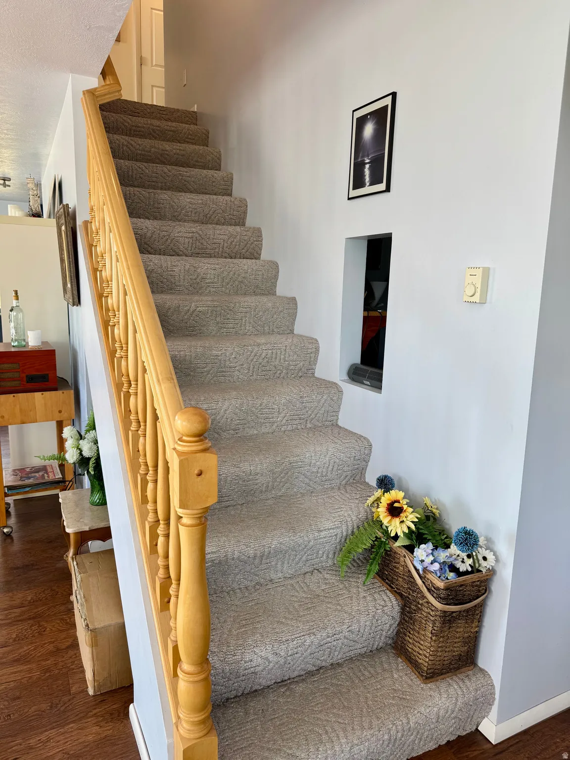 Carpeted staircase with light-toned wood-finish handrail and balusters, featuring a wall niche