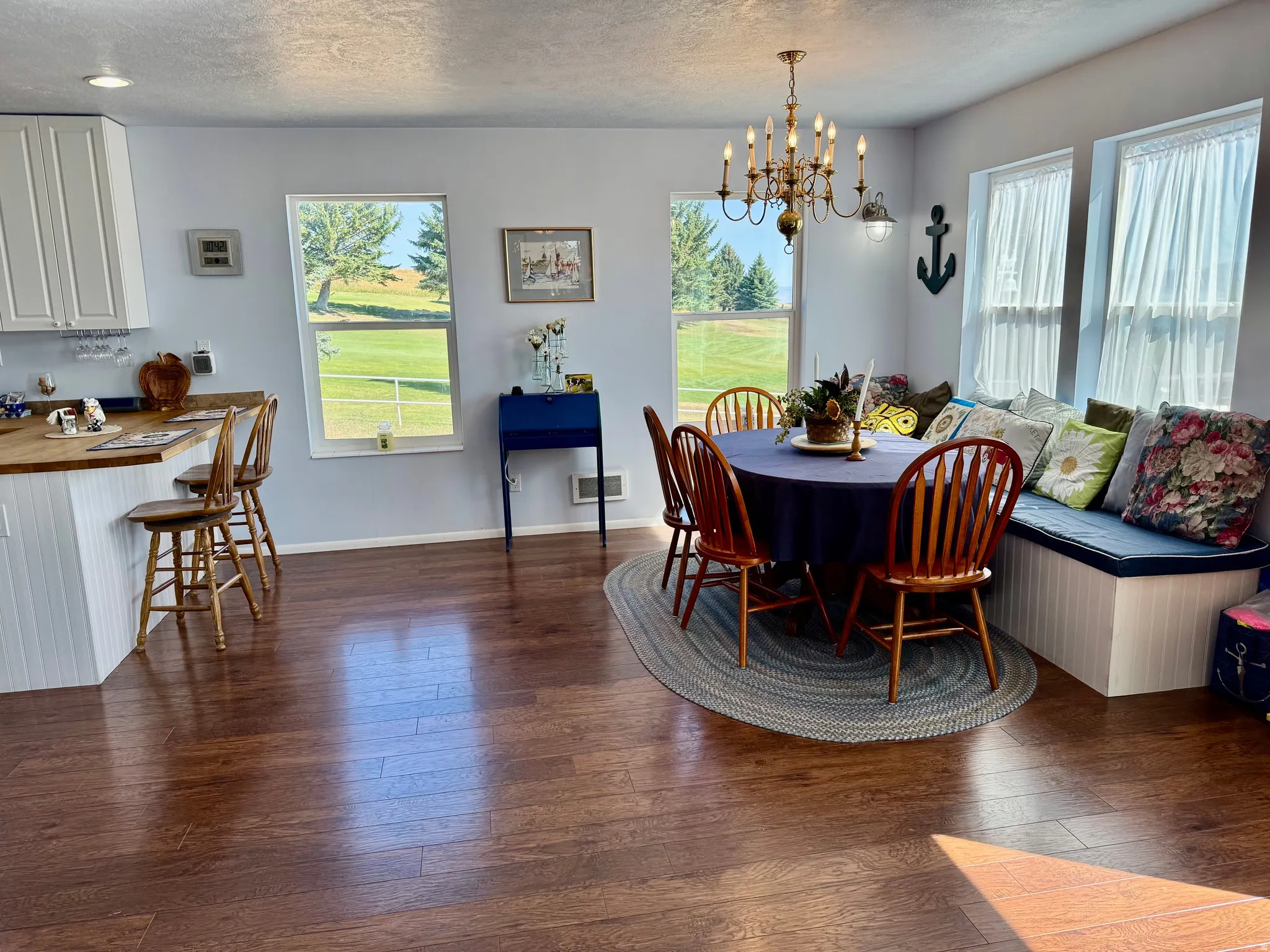 Wood-finish flooring throughout, white cabinetry with wood countertops, built-in window seating, multiple windows, and an antique-style chandelier
