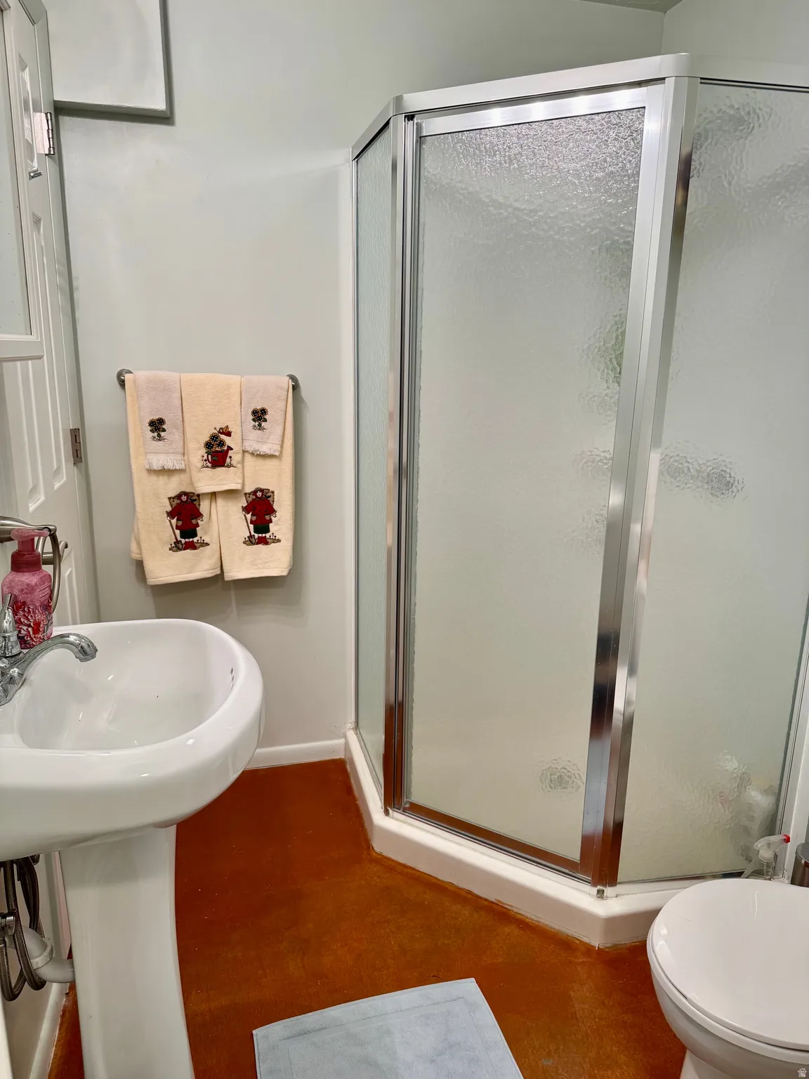 Lower-level 3/4 bath with Pedestal sink, corner shower enclosure with textured glass, and a white toilet