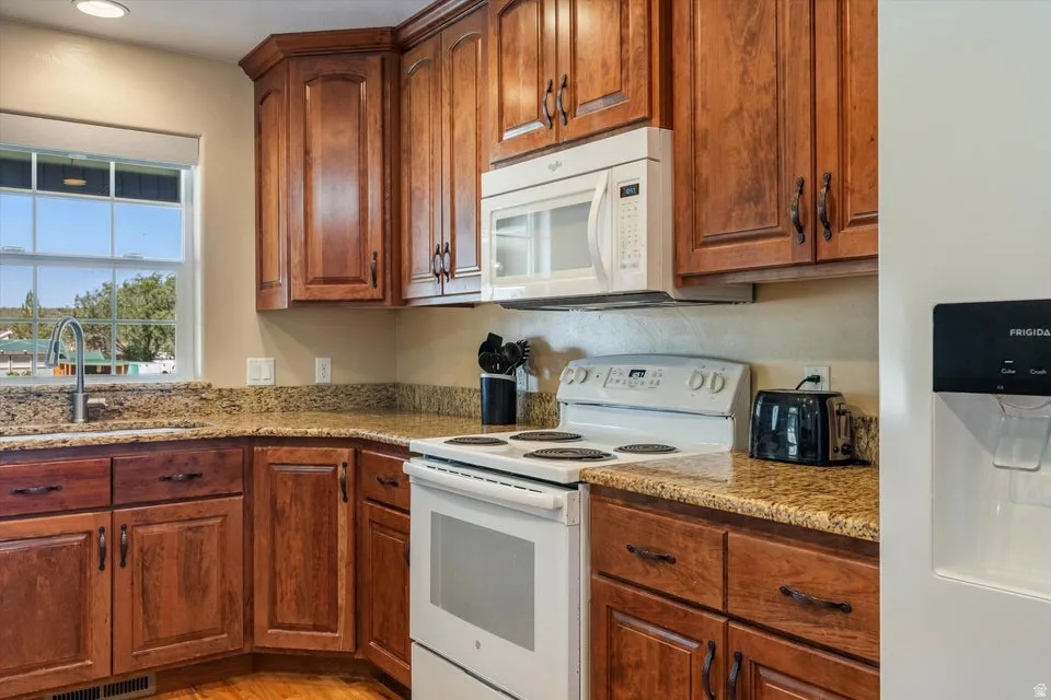 Kitchen featuring wood-finish cabinetry, speckled countertops, a built-in microwave, an electric range, and a stainless steel sink with a gooseneck faucet
