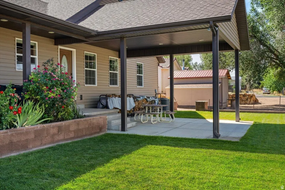 Covered patio with concrete flooring, supported by dark posts, adjacent to a manicured lawn