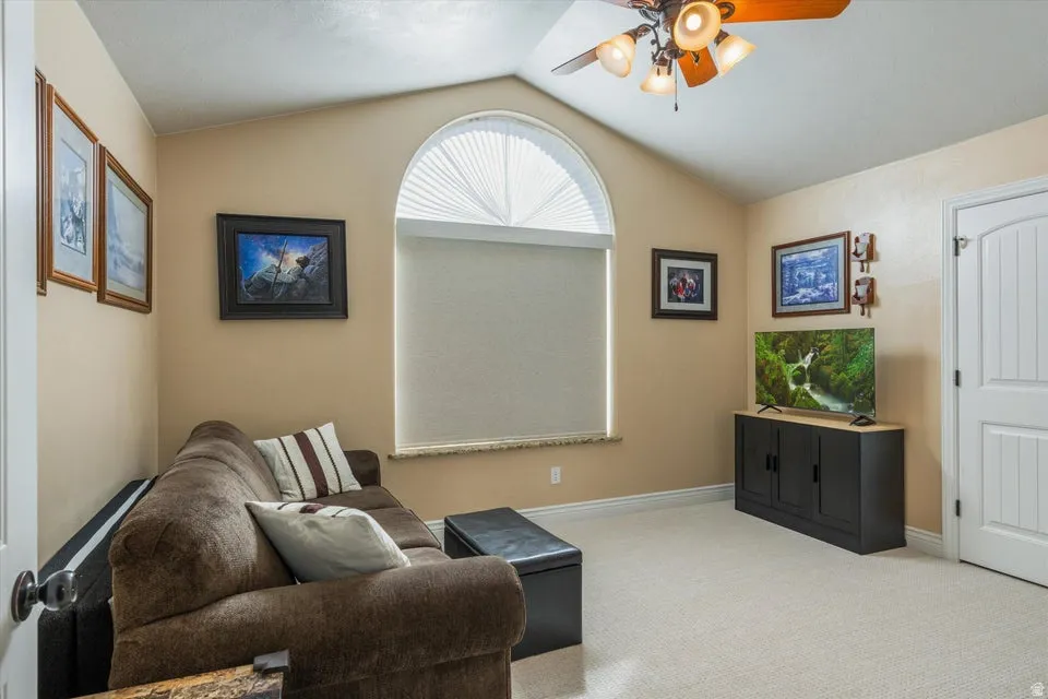 Arched window with privacy blind, sloped ceiling, ceiling fan with integrated lighting, carpeted flooring, and a paneled interior door